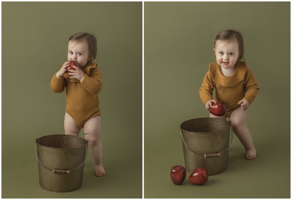 Portrait of toddler girl in knit mustard romper in with bucket of apples.