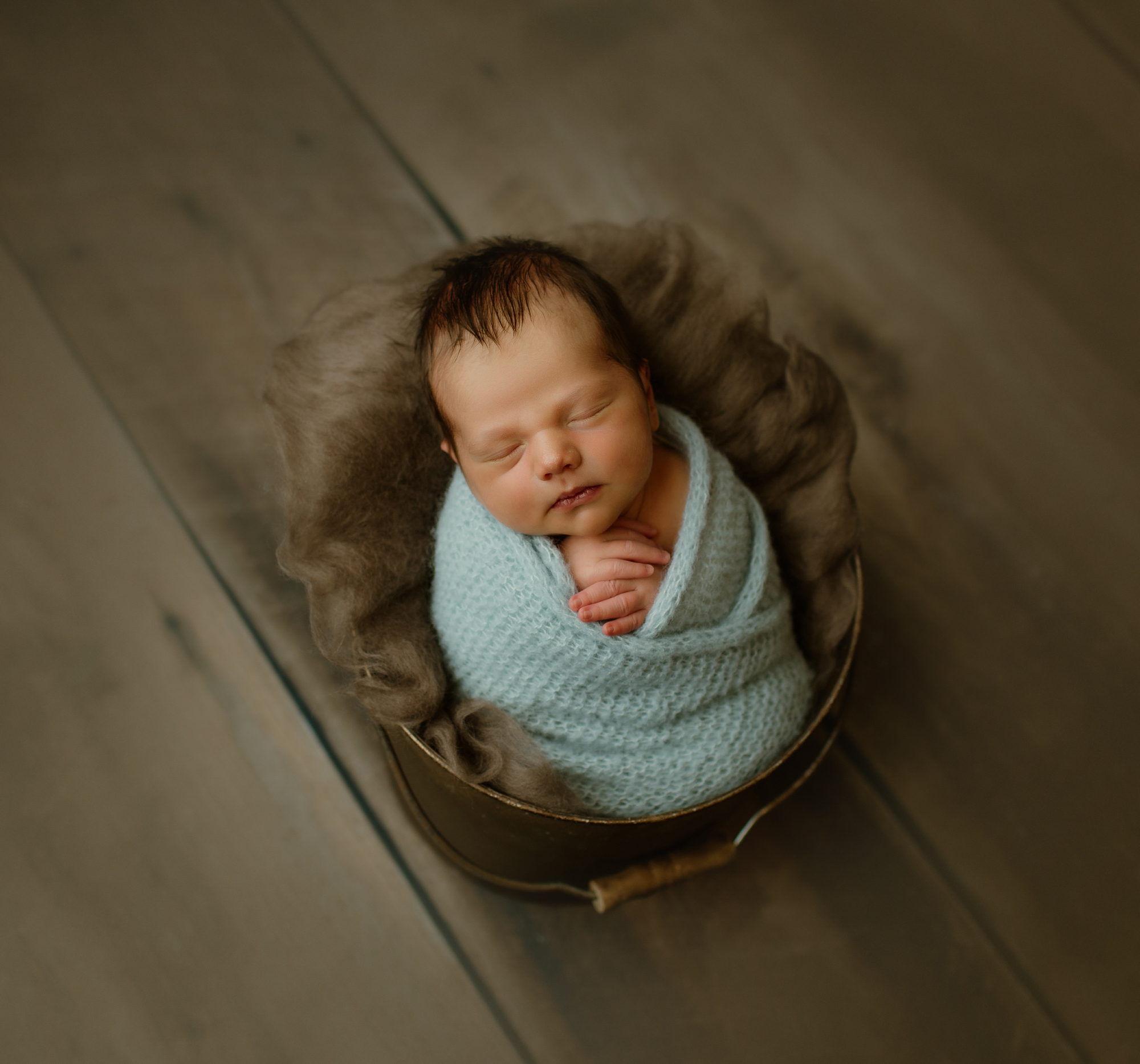 Newborn portrait of baby in blue knit wrap and bucket