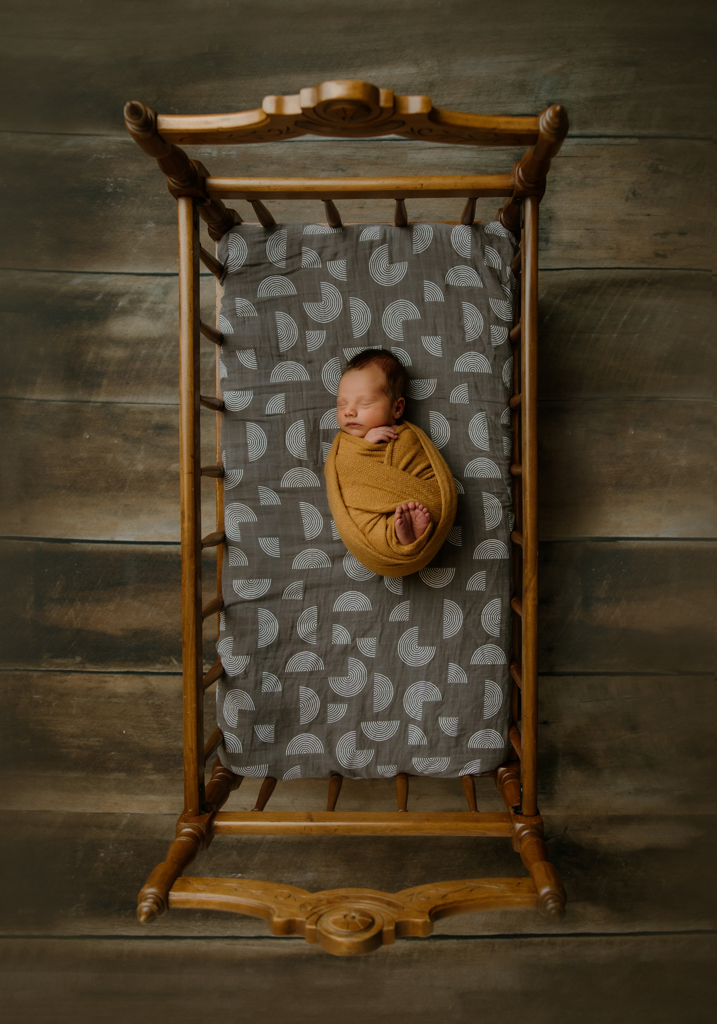 Newborn portrait of baby in yellow knit wrap in antique crib