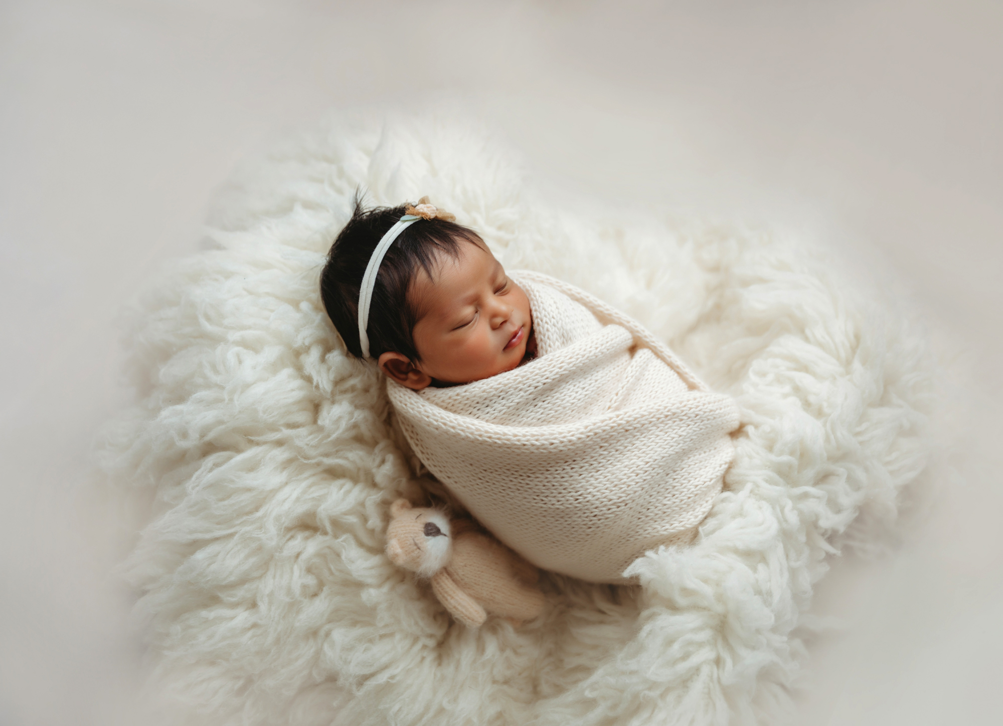Newborn portrait of baby in white knit wrap on flokati