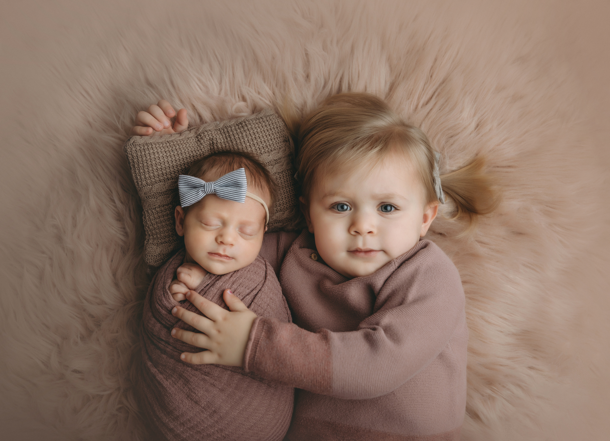Sister and newborn portrait on furry pink blanket