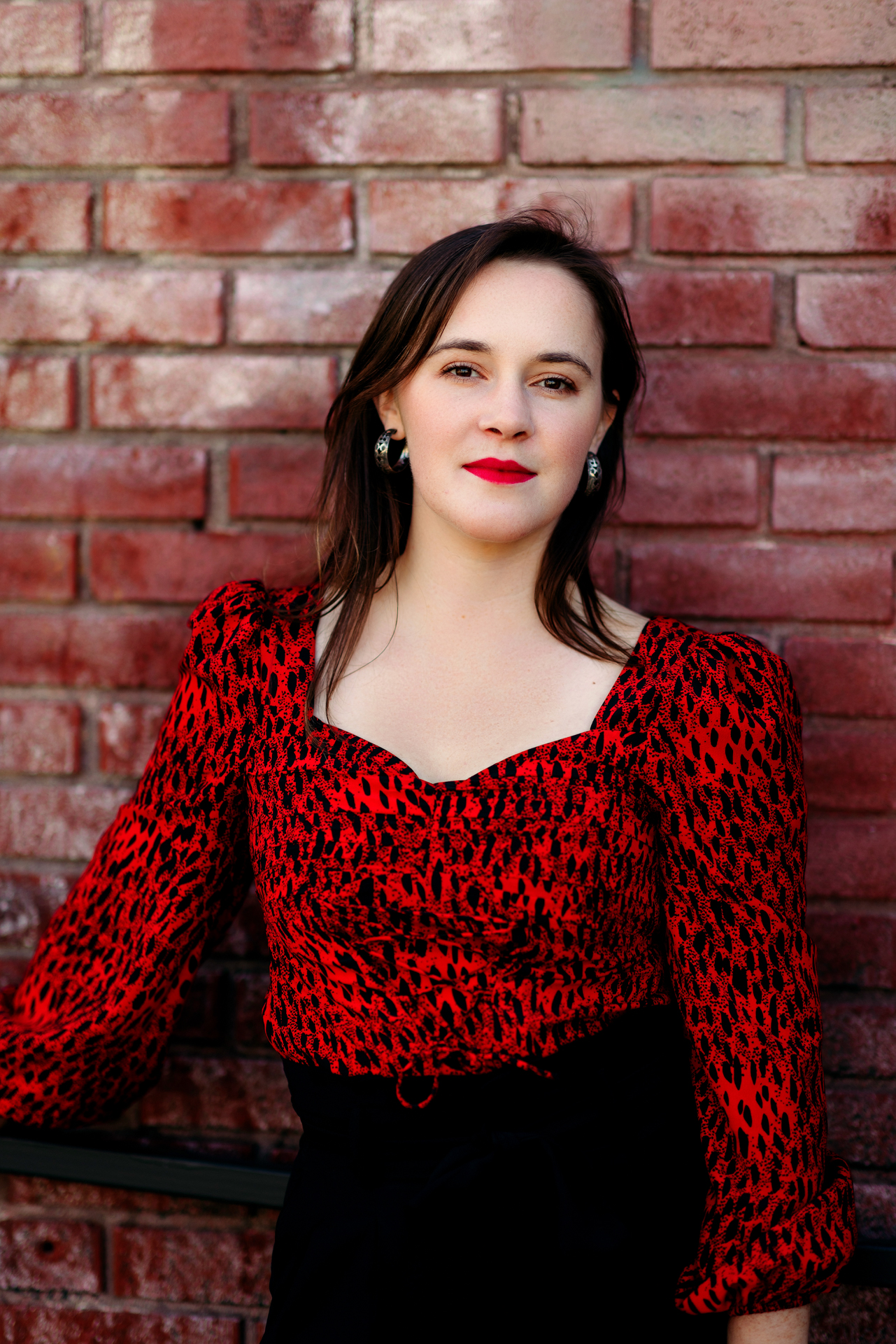 Professional actor headshot of young woman with red shirt against brick wall