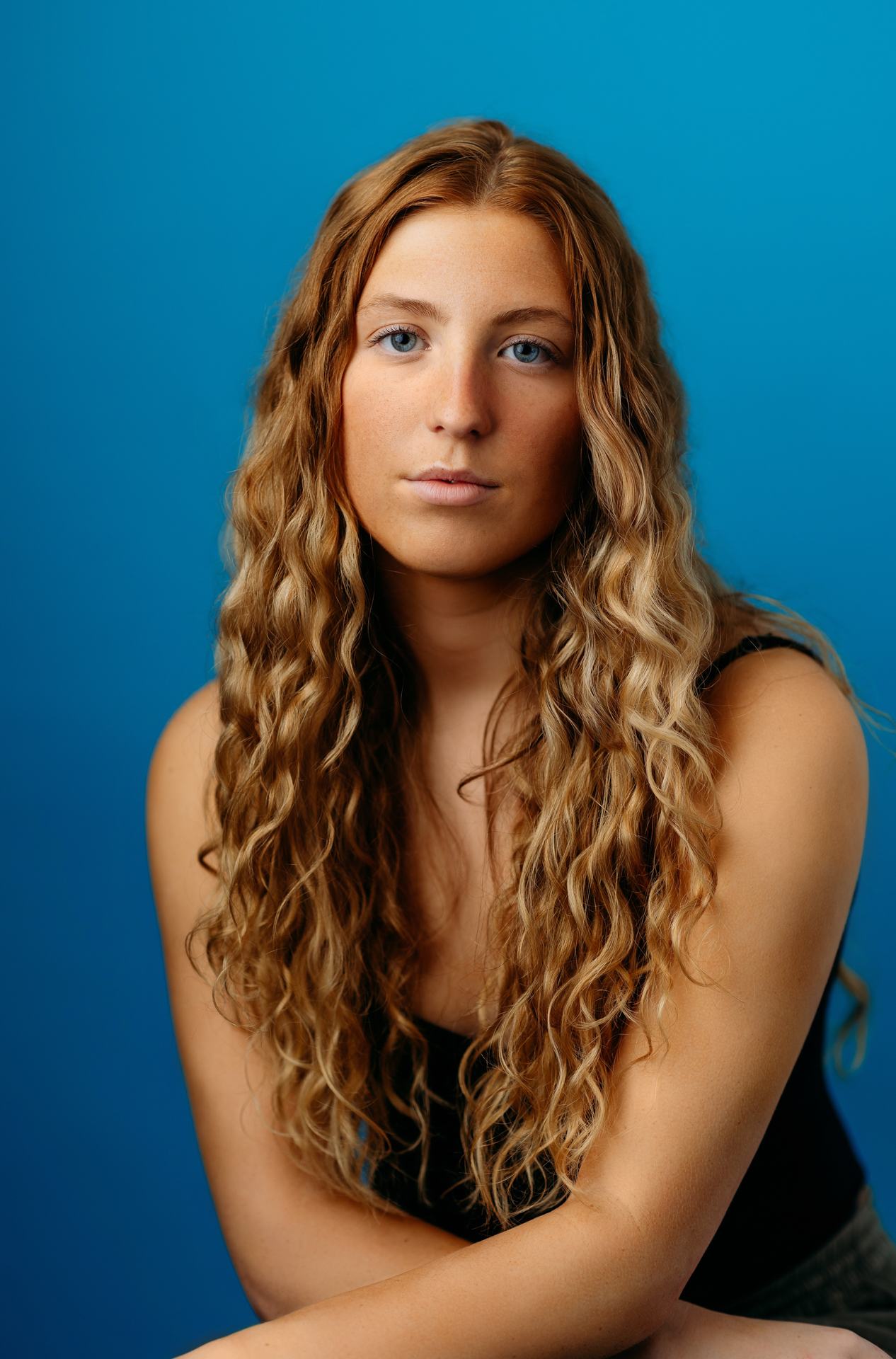 Professional actor headshot of young woman with long curly strawberry blond hair on bright blue background