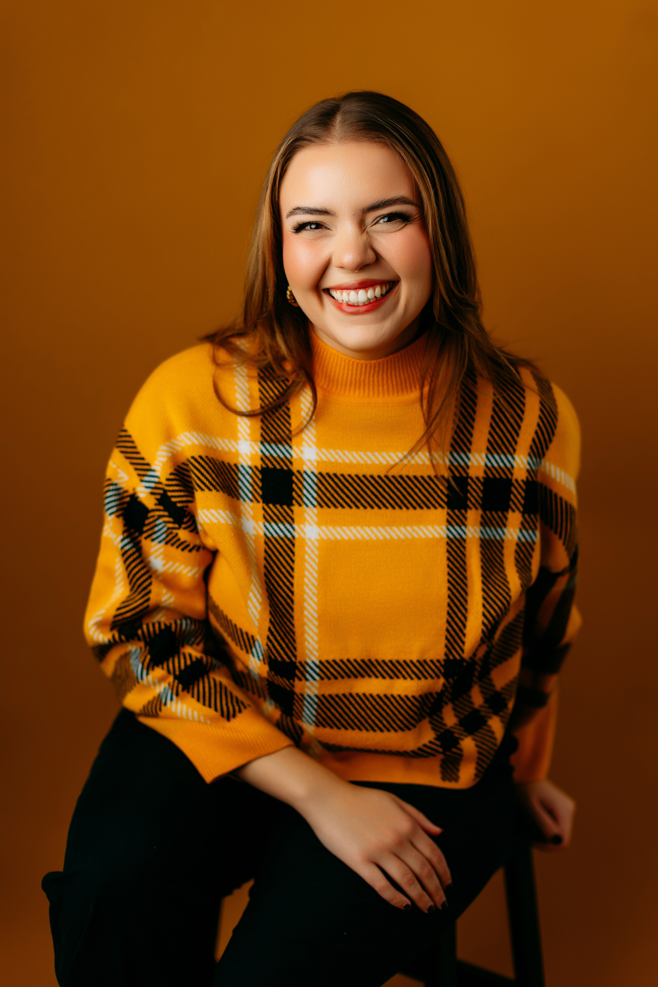 Professional headshot of smiling young woman in black and yellow sweatshirt and deep yellow background