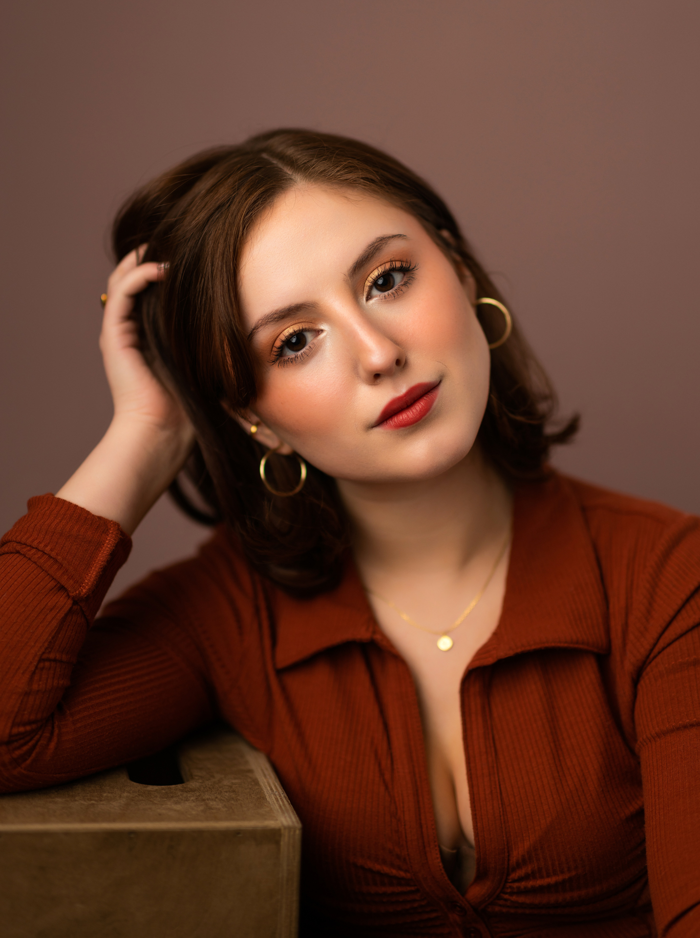 Professional musician headshot of young woman in burnt orange shirt on mauve background