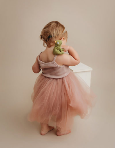 Toddler in pink dress plays with toy frog